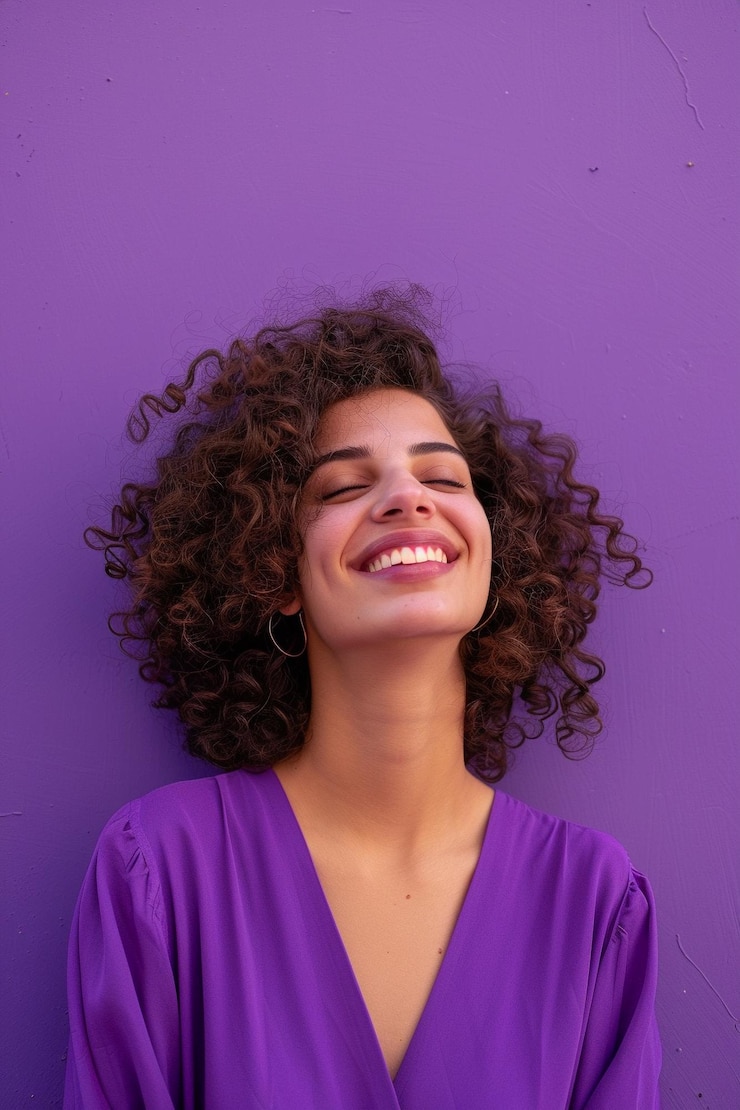 Foto uma mulher com cabelo encaracolado e uma camisa roxa está sorrindo