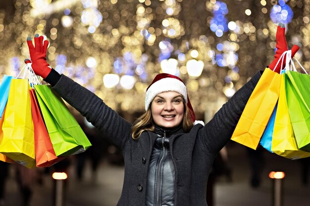 Foto uma mulher com cabelos longos e um chapéu de santa com compras em sacos de papel coloridos compras de ano novo