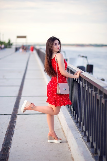 Uma mulher com cabelos longos em um vestido vermelho de verão caminha ao longo do aterro