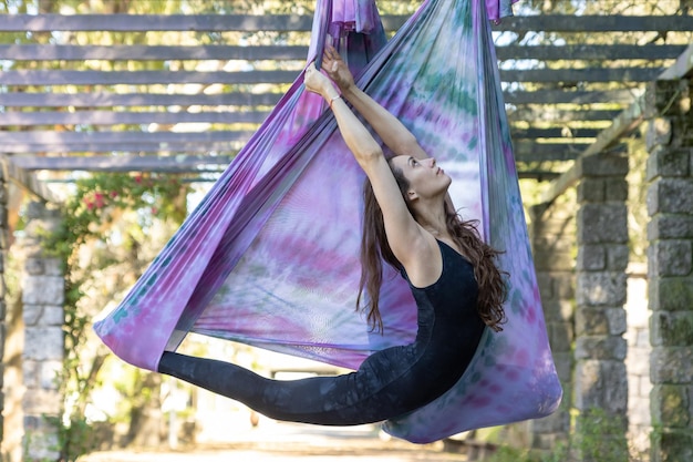 Uma mulher com cabelos longos esticando na rede de ioga com a cabeça erguida