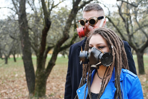 Uma mulher com dreadlocks e uma máscara de gás e um homem com óculos steampunk e uma máscara de gás