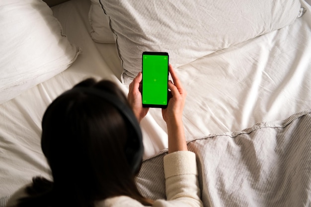 Uma mulher com fones de ouvido deita-se e segura um telefone celular preto com uma tela verde ereta