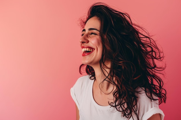 Uma mulher com longos cabelos cacheados rindo e sorrindo em um fundo rosa