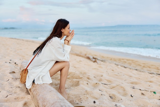 Uma mulher com longos cabelos molhados depois de nadar senta-se na areia de costas para a câmera e olha para o pôr do sol à beira-mar na ilha de Bali