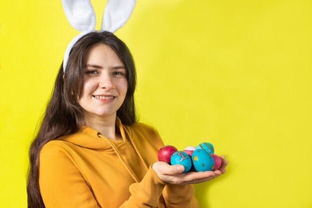 Uma mulher com orelhas de coelho na cabeça segura ovos de páscoa e sorrisos