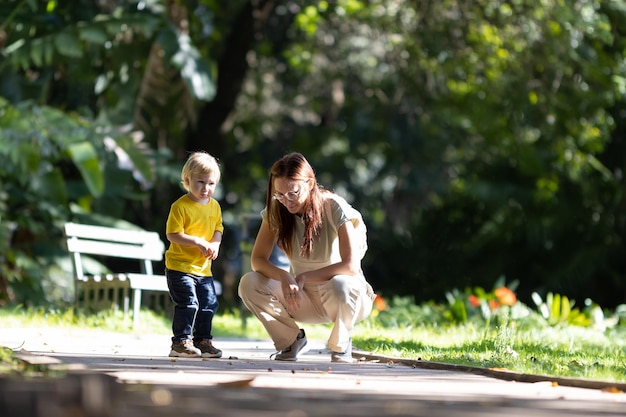 Uma mulher com seu filhinho loiro nas mães do parque olhando para o chão