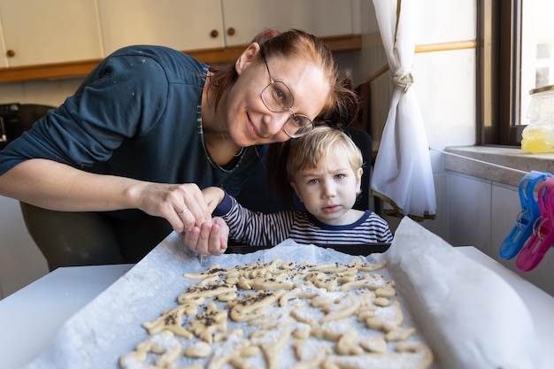 Foto uma mulher com seu filho pequeno faz biscoitos em forma de dinossauros olhando para a câmera