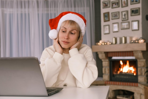 Uma mulher com um chapéu de papai noel parabeniza parentes e amigos em um laptop com o ano novo de natal