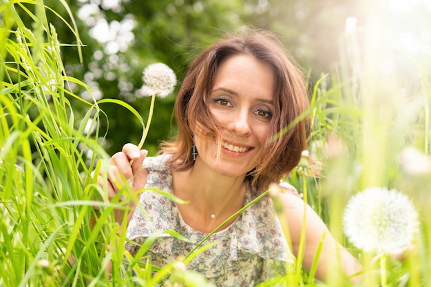 Uma mulher com um dente-de-leão na natureza. Mulher feliz caminhando no parque.