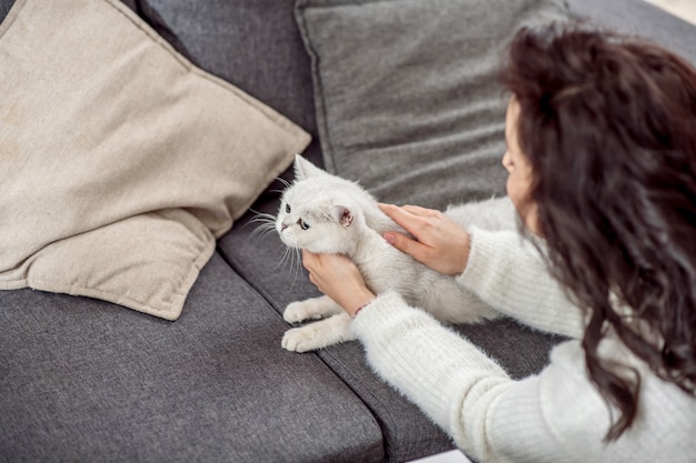 Uma mulher com um gato. Jovem mulher de cabelos escuros passando um tempo com seu lindo gato branco em casa