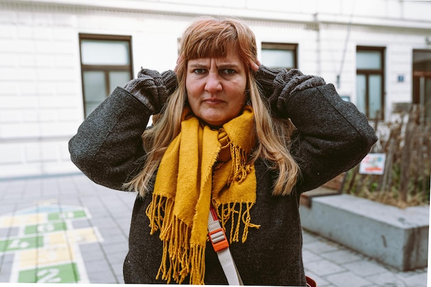 Uma mulher com um lenço amarelo fica em frente a um prédio branco.