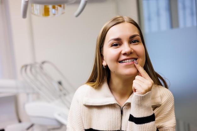 Uma mulher com um sorriso no rosto com aparelho nos dentes está esperando no consultório odontológico por seu médico. Armário em uma clínica odontológica moderna