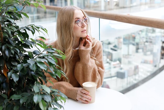 Uma mulher com um suéter confortável em um shopping tomando café