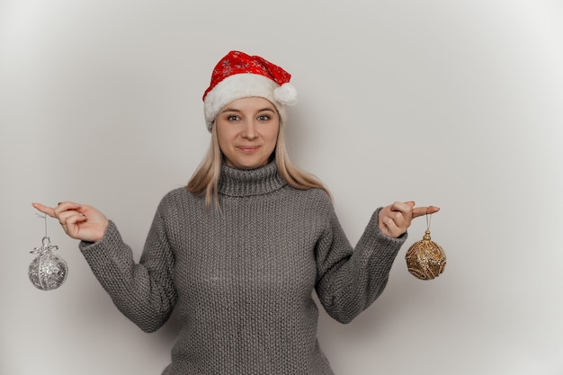 uma mulher com um suéter de lã cinza e um chapéu de Papai Noel segurando decorações de Natal nas mãos