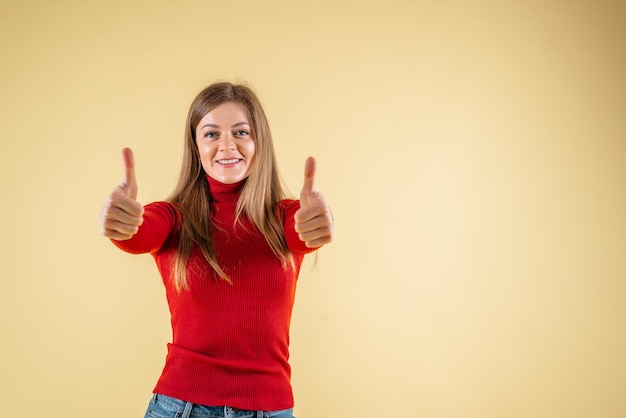 Uma mulher com um suéter vermelho e jeans levanta o polegar.