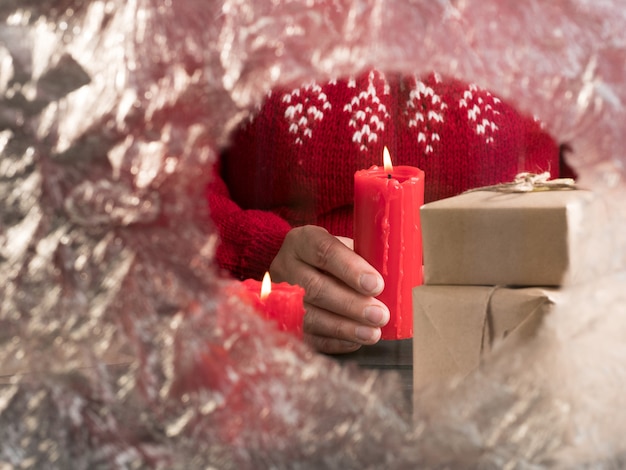 Uma mulher com um suéter vermelho segura uma vela atrás de um vidro congelado. férias de natal.