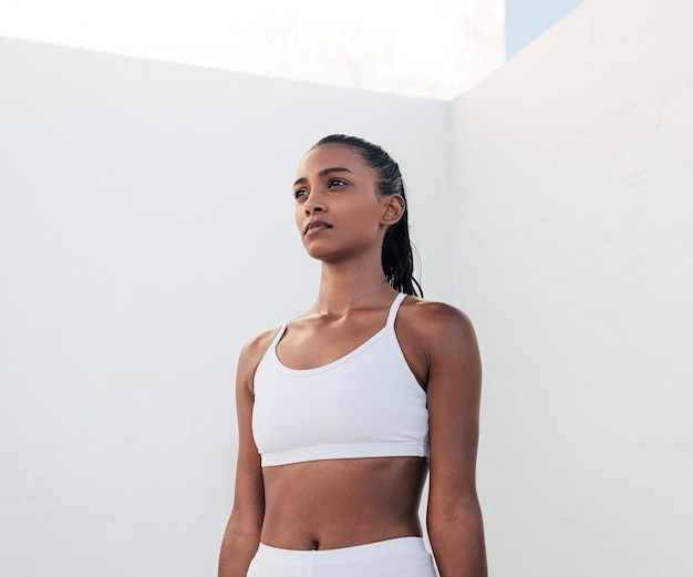 Uma mulher com um sutiã esportivo branco fica em frente a uma parede branca.