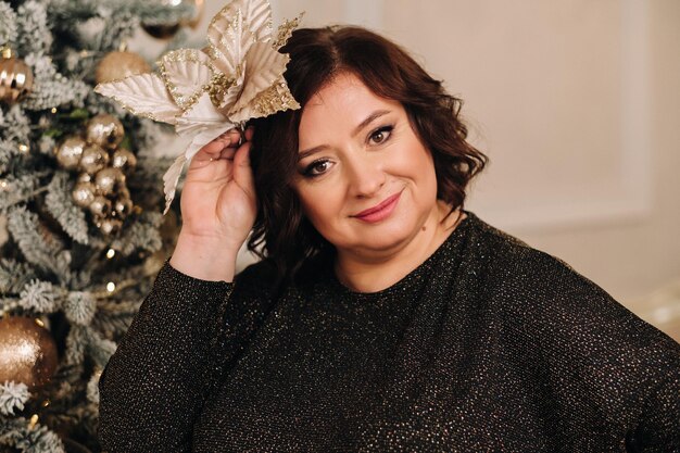 Uma mulher com um vestido escuro ao lado de uma árvore de Natal em um interior projetado para celebrar o Natal e o Ano Novo