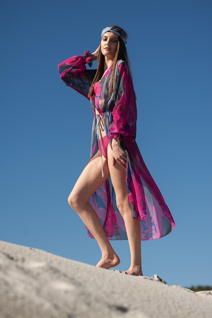 Uma mulher com um vestido listrado fica em pé sobre uma rocha em frente a um céu azul.