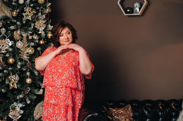 Uma mulher com um vestido vermelho ao lado de uma árvore de Natal em um interior decorado para celebrar o Natal e o Ano Novo