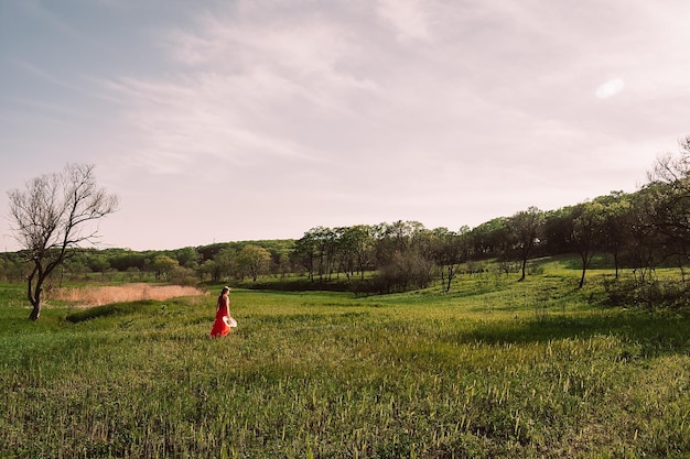 Uma mulher com um vestido vermelho caminha por um campo de grama verde.