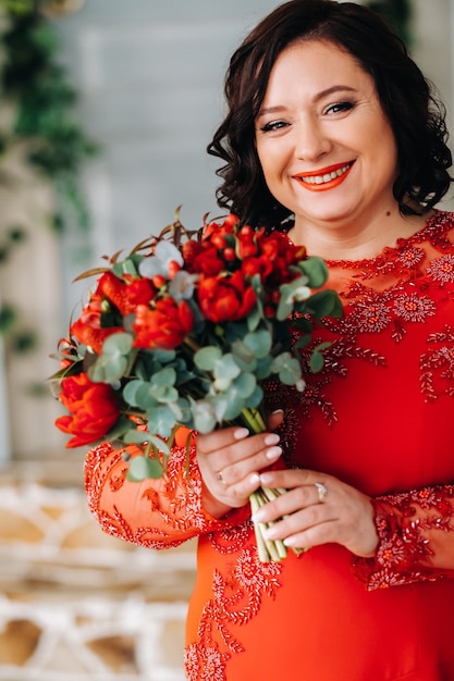 Uma mulher com um vestido vermelho se levanta e segura um buquê de rosas vermelhas e morangos no interior.