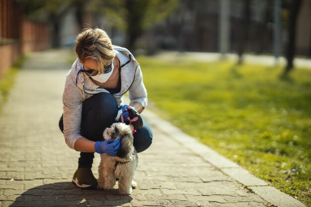 Uma mulher com uma máscara de proteção médica está andando pelo caminho da rua da cidade com seu querido e fofo cachorro Shih Tzu durante o surto de vírus da gripe e epidemia de coronavírus.