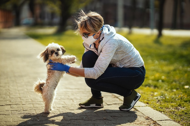 Uma mulher com uma máscara de proteção médica está passando tempo com seu querido e fofo cachorro Shih Tzu