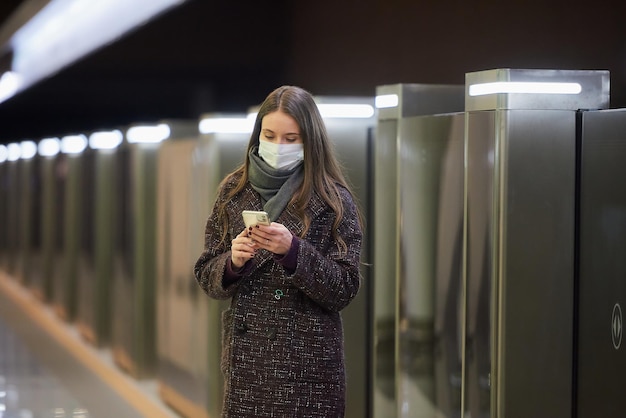 Uma mulher com uma máscara facial médica para evitar a propagação do coronavírus está usando um smartphone