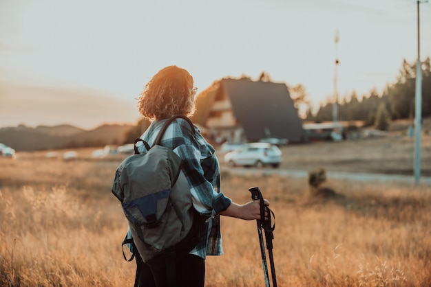 Uma mulher com uma mochila nas costas e equipamento de montanhismo andando no topo de uma montanha ao pôr do sol