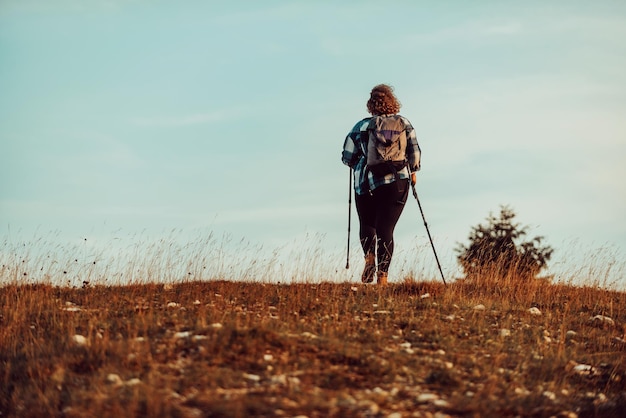Uma mulher com uma mochila nas costas e equipamento de montanhismo andando no topo de uma montanha ao pôr do sol