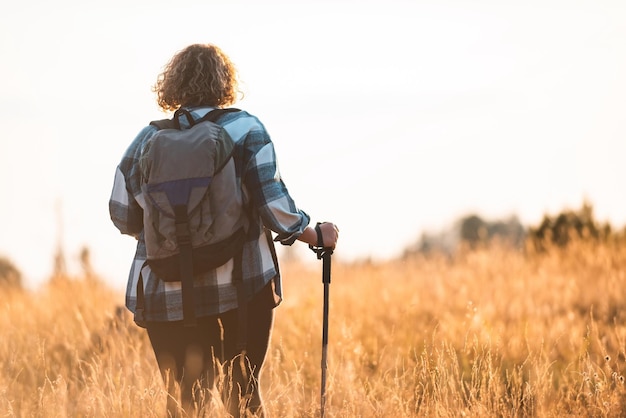 Uma mulher com uma mochila nas costas e equipamento de montanhismo andando no topo de uma montanha ao pôr do sol