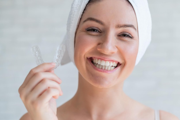 Uma mulher com uma toalha na cabeça segura um protetor bucal clareador para os dentes A menina alinha os dentes com a ajuda de retentores removíveis noturnos transparentes Aparelho ortodôntico para um sorriso perfeito