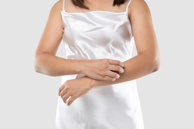 Uma mulher com vestido de cetim branco está coçando os braços devido a coceira em um vestido cinza