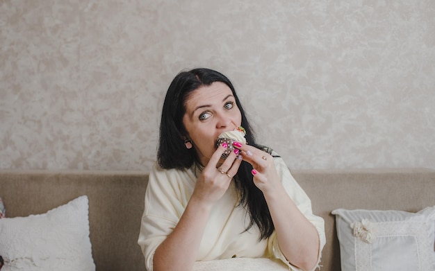 Uma mulher come um delicioso bolinho de morango sentada em casa no sofá e