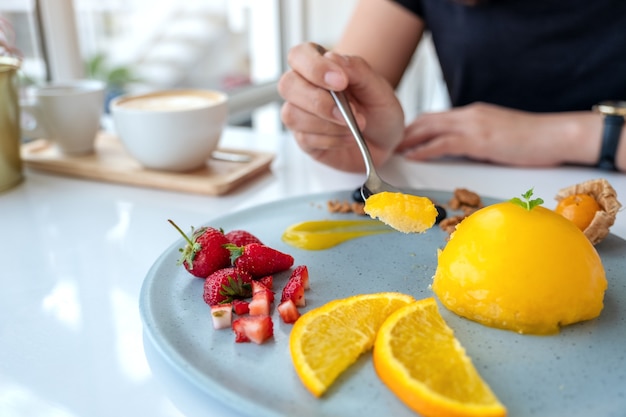 Uma mulher comendo bolo de laranja com uma mistura de frutas por colher em um café