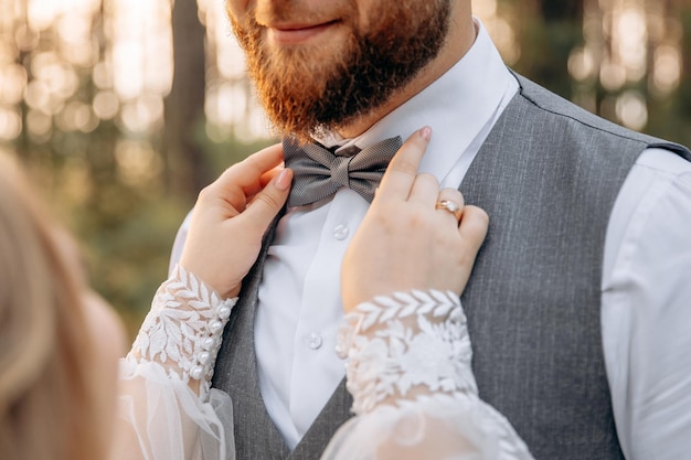 Uma mulher compara uma gravata borboleta ao marido com barba Noiva e noivo estiloso Mãos fechadas