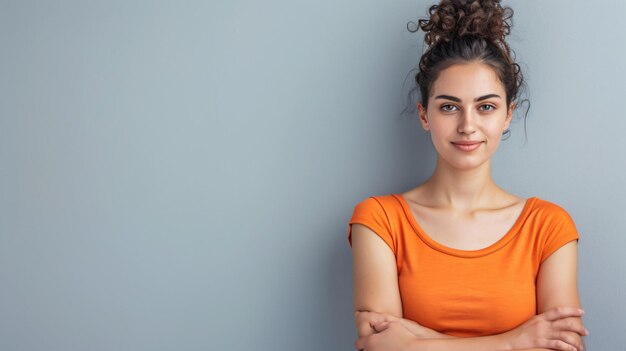 Uma mulher confiante e radiante exala charme e carisma enquanto ela confidentemente cruza os braços enquanto está vestida com um singlet laranja atraente com um fundo cinza isolado esta imagem repr