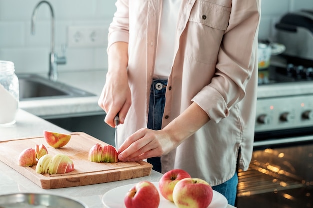 Uma mulher corta maçãs frescas na cozinha para fazer uma torta.