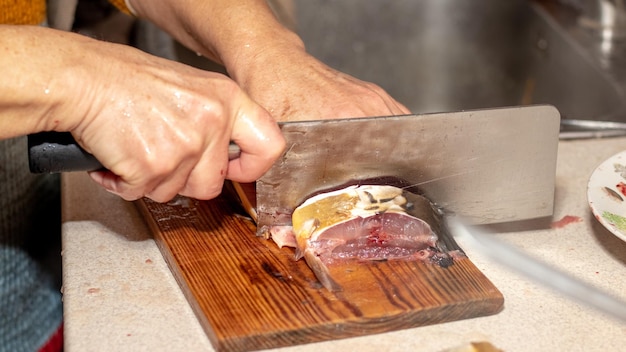 Uma mulher corta peixe com uma faca grande em casa na cozinha