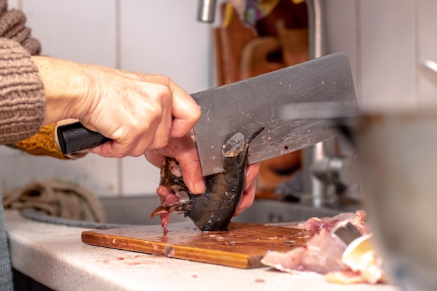 Uma mulher corta peixe com uma faca grande em casa na cozinha