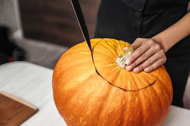 Foto uma mulher corta uma abóbora com uma faca, preparando-se para o halloween, close-up, vista de cima