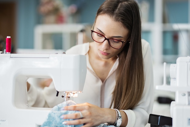 Uma mulher costura na oficina de alfaiates de moda da máquina de costura elétrica