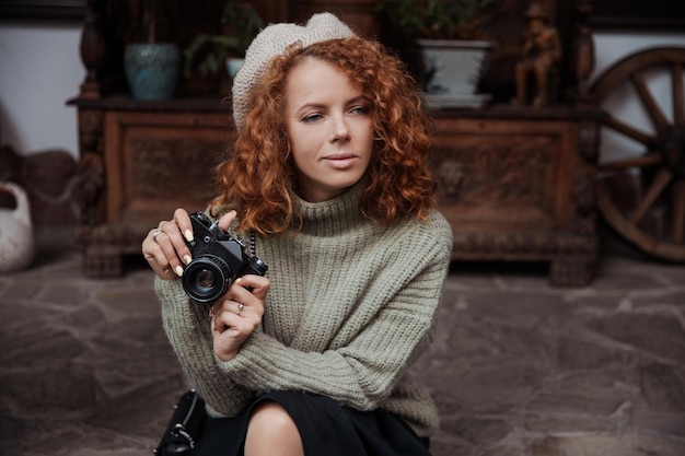 Uma mulher de boina e suéter verde segura uma câmera nas mãos e tira fotos