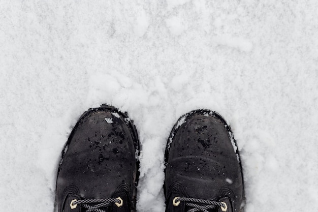 Uma mulher de botas pretas fica na neve no inverno Pernas fechadas