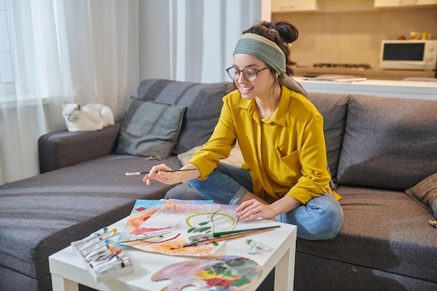 Uma mulher de camisa amarela pintando e parecendo envolvida