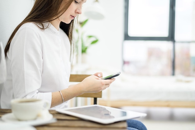 Uma mulher de camisa branca está bebendo café em um café Uma trabalhadora de escritório no intervalo do almoço resolve um problema de negócios por telefone Gerente de nível médio