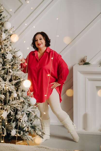 Uma mulher de camisa vermelha em uma sala perto de uma árvore de Natal decorada para a atmosfera de Natal em casa de Ano Novo