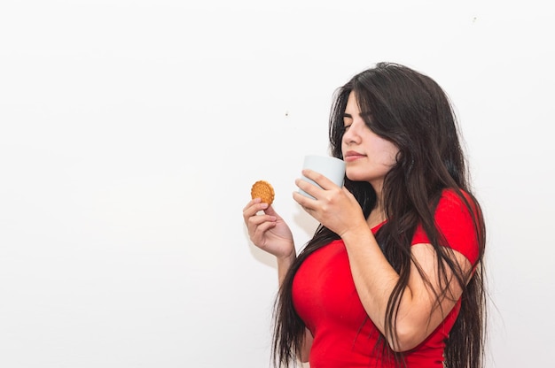 Foto uma mulher de camisa vermelha está segurando um biscoito e desviando o olhar.