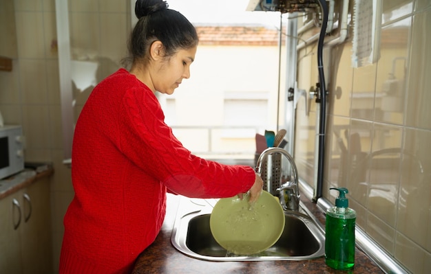 Uma mulher de camisola vermelha está lavando um prato em uma pia